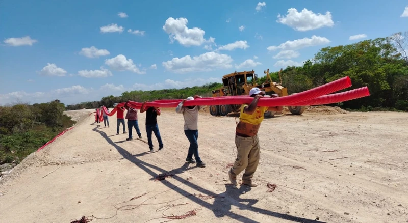 Cuadrilla trasladando tubo corrugado rojo para los ductos del Tren Maya